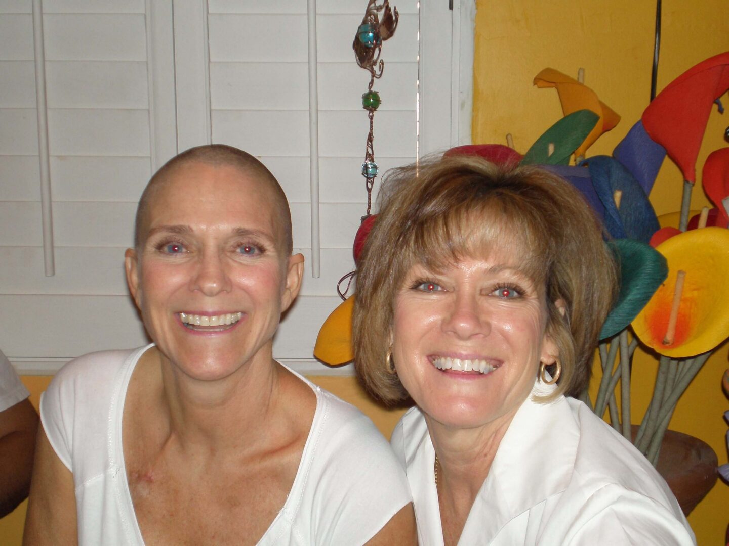Two smiling women in front of colorful flowers.
