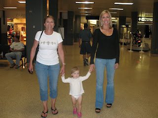 Two women holding toddler's hands in airport