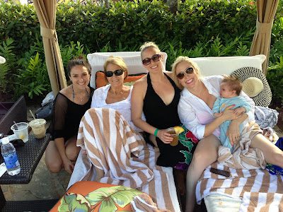 Four women lounging poolside, one holding baby