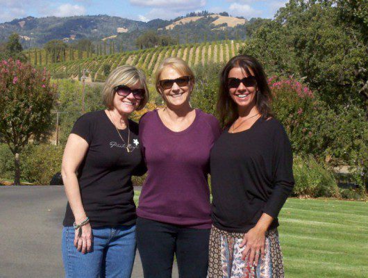 Three women diagnosed with ovarian cancer posing for a picture in front of a vineyard.