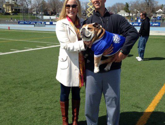 A man and woman posing with a bulldog on a field.