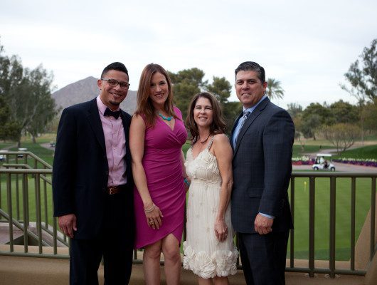 Four people posing outdoors on balcony.