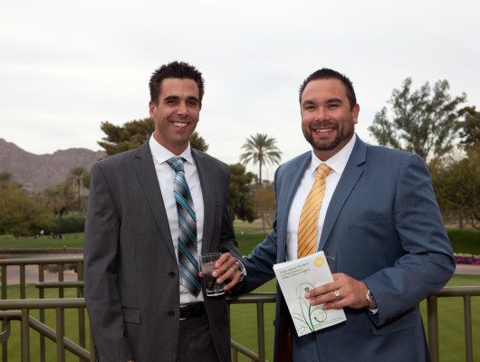 Two men in suits outdoors, smiling.