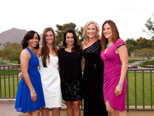 Five women posing in colorful dresses outdoors.