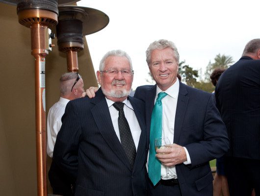 Two men smiling at outdoor event.