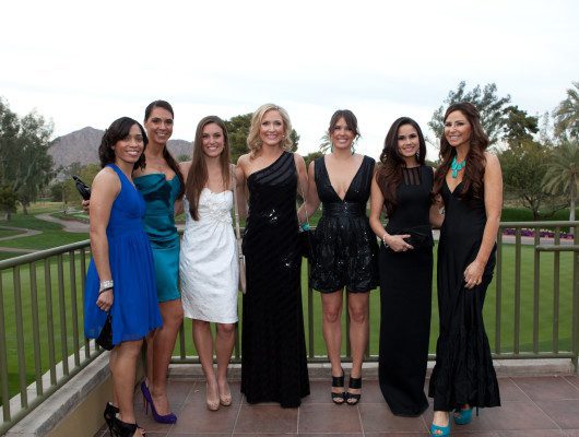 Seven women in elegant evening dresses outdoors.