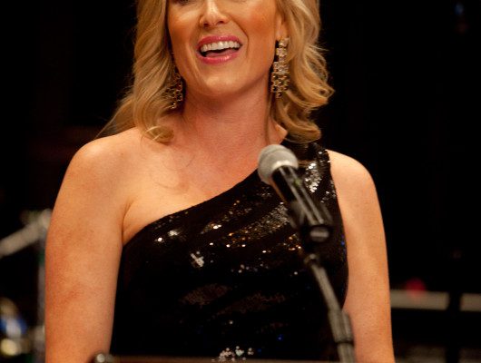 Woman speaking at a podium, wearing black dress.