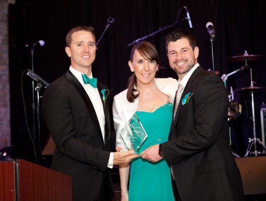 Three people holding an award on stage.