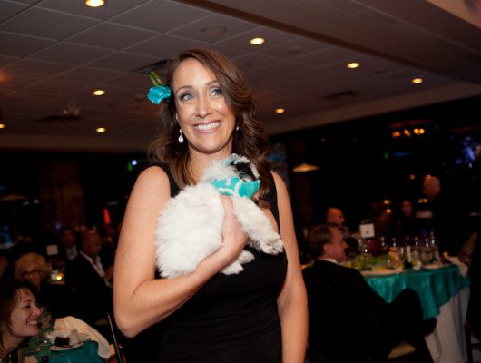 Woman holding a fluffy white dog indoors.