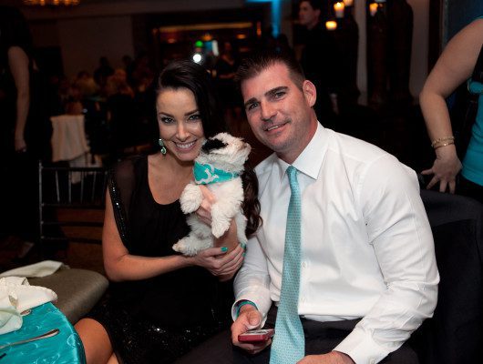 Couple smiling with small dog at event.