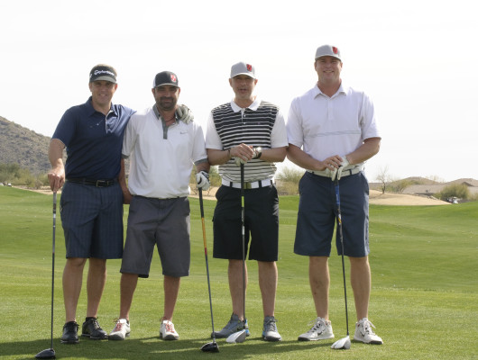 Four men posing with golf clubs outdoors.