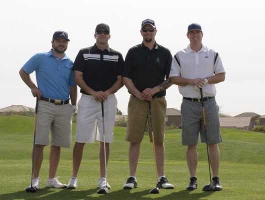 Four men posing on a golf course.