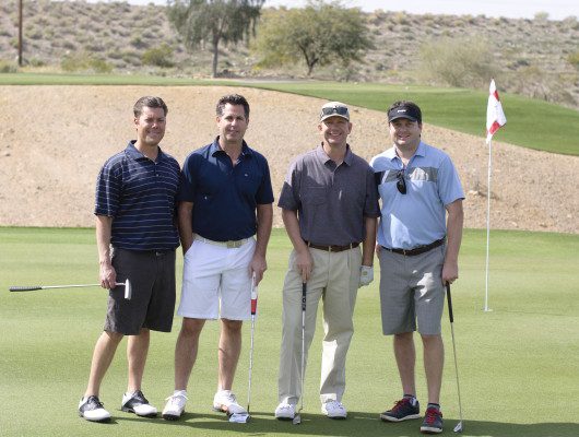 Four men posing on a golf course.
