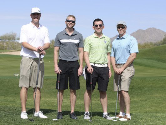 Four men posing on a golf course.