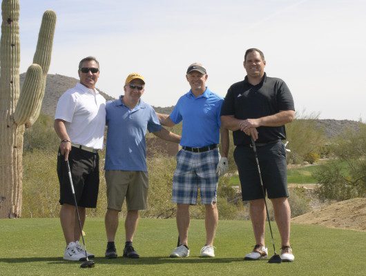 Four men posing on a golf course.