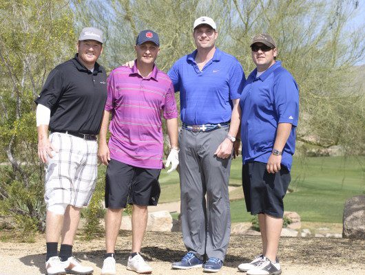 Four men posing on a golf course.