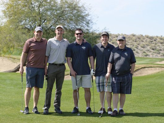 Five men standing on a golf course.