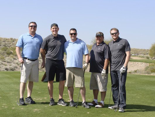 Five men standing on a golf course.
