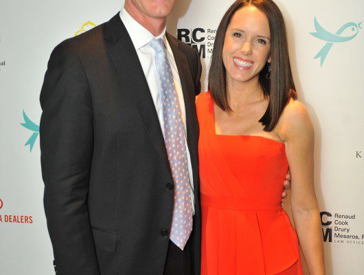 Man and woman smiling at event backdrop.