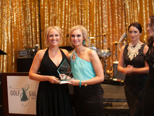 Two women holding an award on stage.