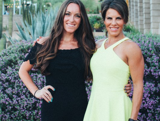 Two women posing outdoors in bright dresses.