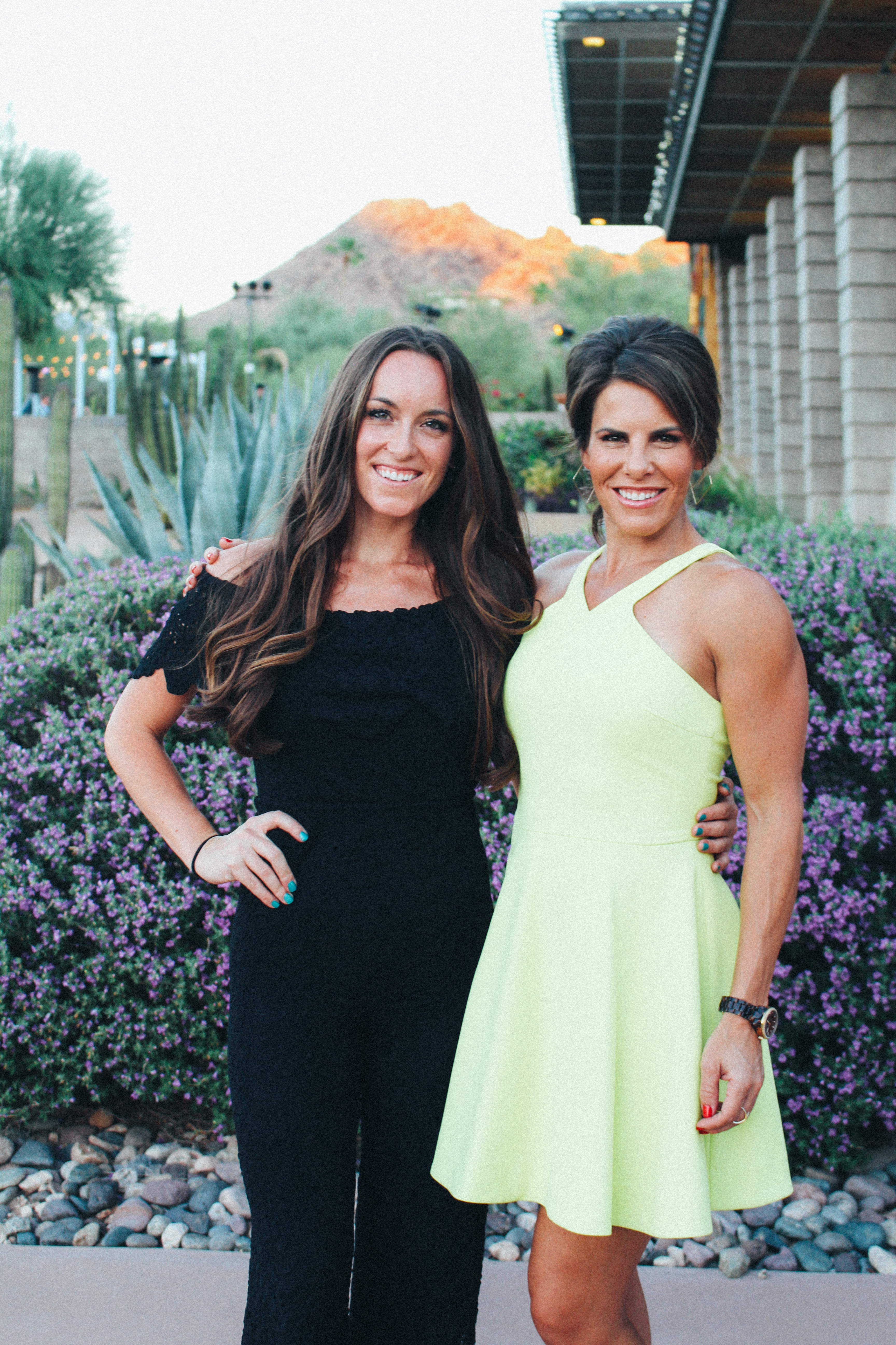 Two women posing outdoors in bright dresses.
