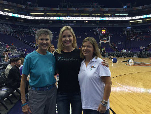 Three women smiling in a sports arena.