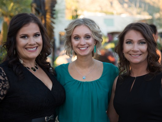 Three women smiling at outdoor event.