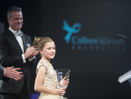 A young girl is holding an award at an awards ceremony.