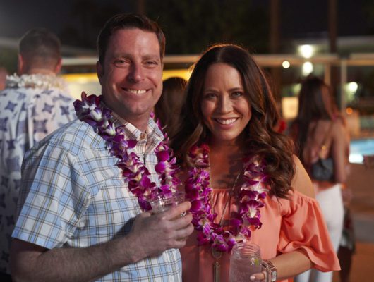 Smiling couple wearing leis at outdoor event.